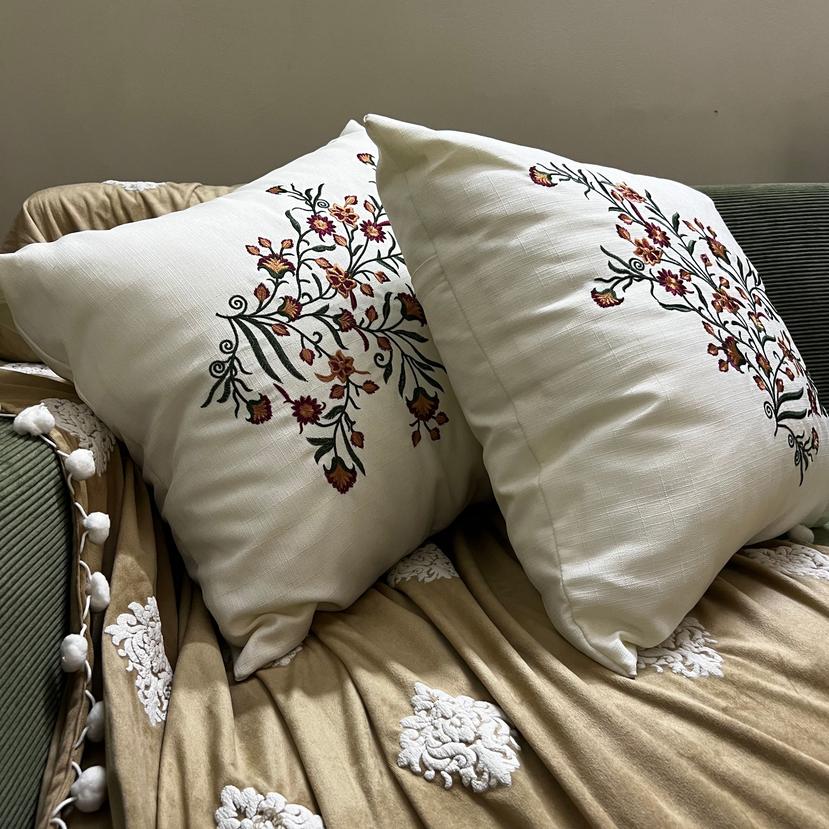 A green sofa with a brown Sofa throw and Cushions with red embroidary 