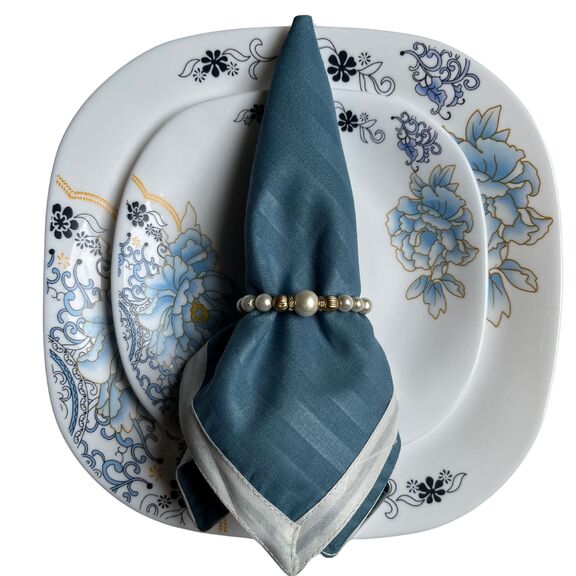 The blue Napkin with white borders wrapped up with a fancy napkin ring is kept on a plate